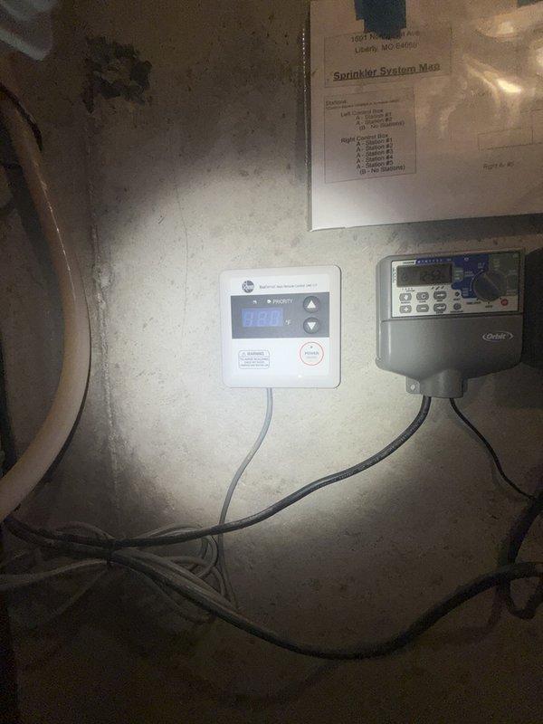 Responded to reported leak originating from above tankless water heater system in basement. Upon inspection, identified the source as plumbing connections associated with the water heater manifold assembly featuring copper and brass piping with T-junction fittings and a blue flexible supply line. Examined all visible pipe connections, valves, and fittings in the vicinity of the digital control units and water heater system. Performed leak detection assessment of the piping assembly to determine exact location and cause of water intrusion, inspecting both the horizontal and vertical pipe runs along with associated shut-off valves and connection points.
