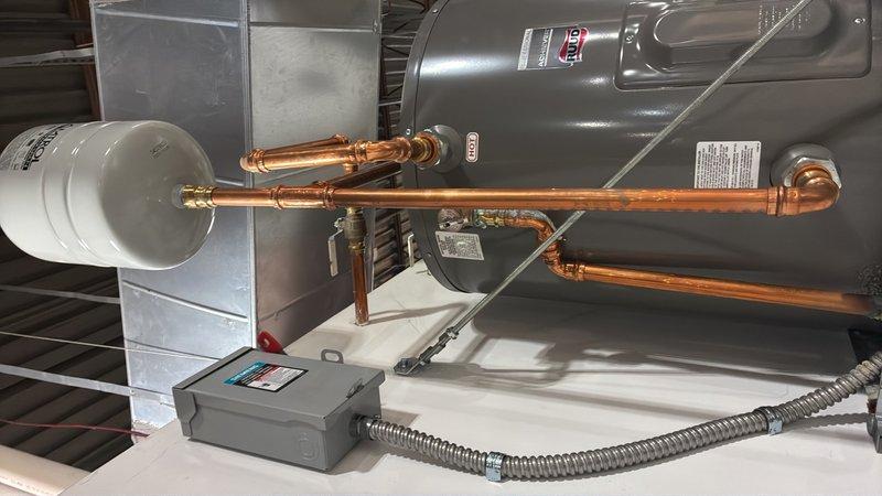 Conducted commercial plumbing estimate for 19-gallon electric water heater replacement at warehouse facility. Accessed elevated unit above back office door using ladder provided by customer, inspected existing 3-year-old electric water heater with copper supply lines, expansion tank, and electrical disconnect box. Unit currently operational; documented installation configuration including piping connections, mounting hardware, and mechanical room layout to provide replacement specifications.