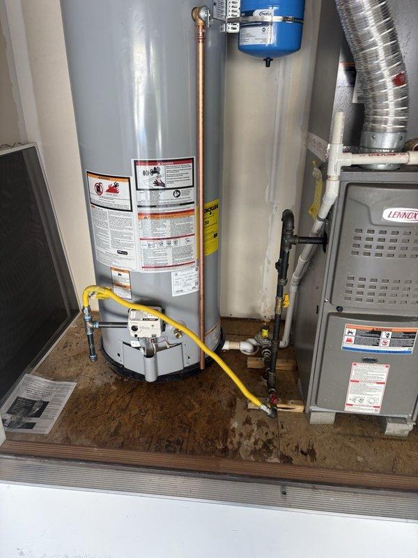 Completed installation of a 50-gallon gas water heater in residential utility closet. Positioned unit on plywood platform alongside existing Lennox HVAC system, connected yellow gas supply line to base of heater, and ran copper piping from top of unit. Installed blue thermal expansion tank above water heater with proper copper pipe connections to manage thermal expansion and protect plumbing system from excessive pressure. All safety labels, pressure relief mechanisms, and shut-off valves installed per manufacturer specifications and local code requirements.