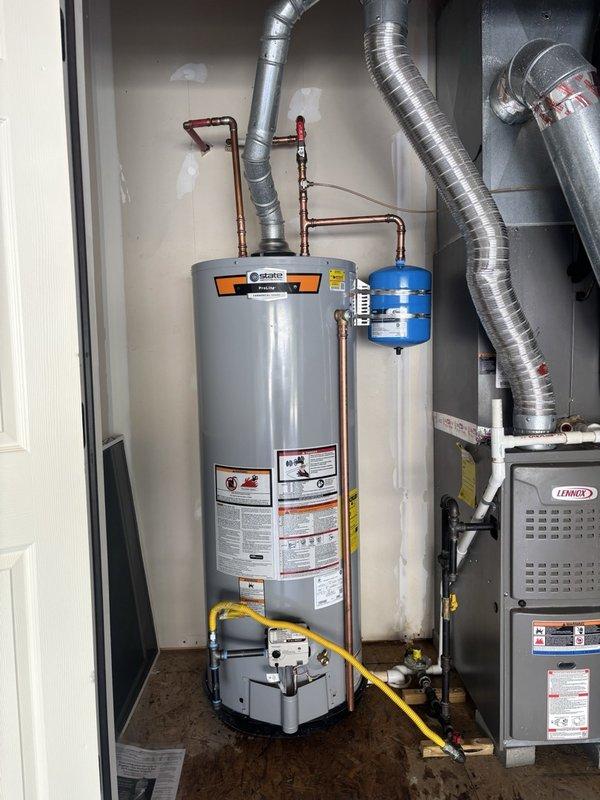 Completed installation of a 50-gallon gas water heater in residential utility closet. Positioned unit on plywood platform alongside existing Lennox HVAC system, connected yellow gas supply line to base of heater, and ran copper piping from top of unit. Installed blue thermal expansion tank above water heater with proper copper pipe connections to manage thermal expansion and protect plumbing system from excessive pressure. All safety labels, pressure relief mechanisms, and shut-off valves installed per manufacturer specifications and local code requirements.