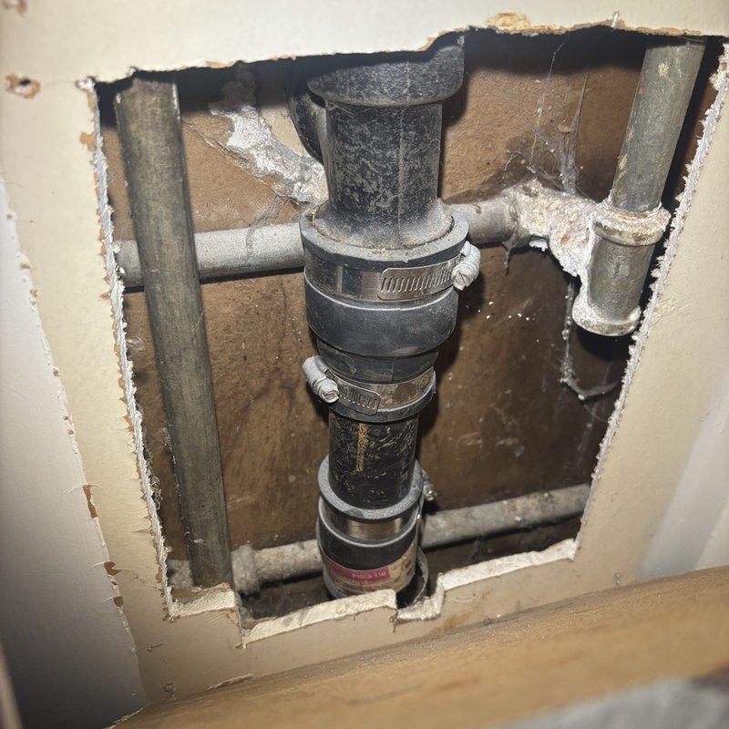 Responded to callback for persistent leak at bathroom sink originally addressed on previous visit. Upon inspection, accessed plumbing behind wall cavity and identified leak source at vertical drain assembly. Leak was caused by compromised connection points on black PVC drain pipe secured with metal hose clamps. Tightened all clamp connections on the vertical waste assembly and horizontal branch lines, inspected flexible supply line connections at wall-mounted fixture, and verified proper seal at all joints. Tested system under full water pressure to confirm leak resolution. Wall access opening left available for final verification before closure.