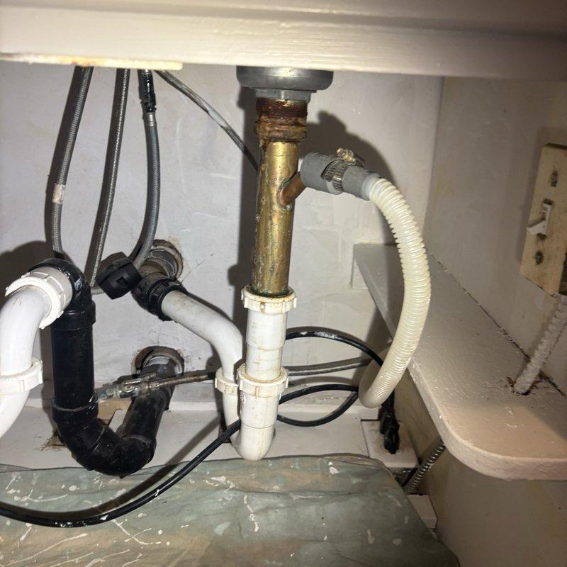 Removed and replaced the existing galvanized kitchen drain line with new PVC piping from the kitchen sink drain connection to the existing ABS transition point. Replaced the kitchen sink P-traps with new PVC components and installed a basket strainer with quick lock connection at the sink drain. Replaced the dishwasher tailpiece to ensure proper connection to the new drain system. Reconnected the kitchen sink drain to the existing vent connection located behind the cabinet wall. Tested all new connections for proper drainage and verified no leaks were present throughout the entire drain assembly.