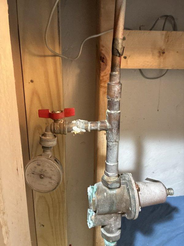 Performed plumbing maintenance inspection on building mechanical systems. Examined HVAC unit connections and verified integrity of braided metal supply lines and flexible conduits with proper fittings and seals. Inspected exposed plumbing assembly in wall cavity, including galvanized pipe fittings, copper supply lines showing oxidation, red-handled shut-off valve, and pressure gauge reading at zero. Documented current condition of all components with photographs for maintenance records.