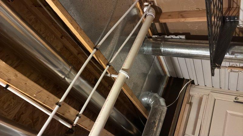 Installed new drain line and water supply lines for secondary kitchen sink. Removed section of drywall on back wall to access stud cavity for pipe installation. Drilled pilot hole through floor to locate connection points in unfinished basement space below. Routed drain line horizontally across basement ceiling joists, connecting to existing main kitchen stack. Ran hot and cold water supply lines from water heater location with dedicated shut-off valves installed for future service access. Temporarily removed HVAC return air panel to facilitate pipe routing through ceiling space. All piping installed to current plumbing code specifications with proper slope on drainage and secure mounting throughout run.