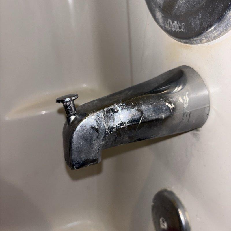 Responded to service call for inoperable shower diverter in main bathroom. Upon arrival, found chrome bathtub spout with stuck diverter knob preventing shower activation. Inspection revealed significant calcium and mineral deposit buildup on spout fixture due to hard water accumulation, which was causing mechanical binding of the diverter mechanism. Documented existing condition showing heavy white crusty deposits concentrated on chrome spout surface. Assessed shower/tub combination unit with standard white porcelain finish and chrome fixtures for repair recommendations.