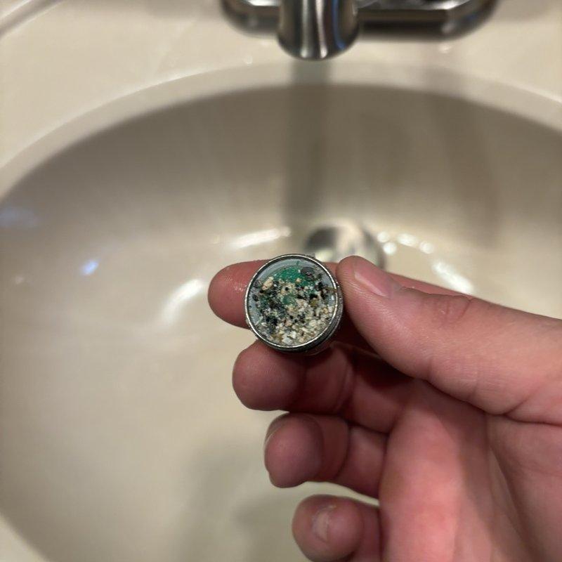 Responded to callback for low water pressure in hall bathroom following previous service visit. Upon inspection, discovered heavily clogged faucet aerator with significant mineral deposits, hard water scaling, and debris buildup restricting water flow. Removed and cleaned aerator, restoring full water pressure to fixture.