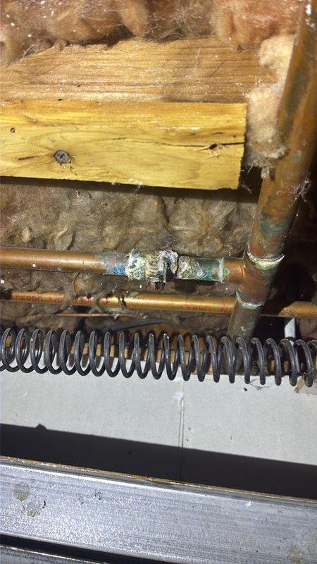 Conducted comprehensive piping assessment for water heater replacement and associated plumbing connections. Documented existing natural gas water heater unit (Model GCVAH03511401) manufactured in August 2019, noting ASME certification and current condition. Evaluated deteriorated copper piping system showing extensive corrosion, white and green oxidation buildup, and mineral deposits indicating prolonged moisture exposure. Inspected HVAC integration points where copper lines interface with heating components and coil assemblies. Photographed corroded pipe sections requiring replacement to prevent potential leaks and system failures. Assessed surrounding infrastructure including fiberglass insulation and structural mounting conditions to determine scope of piping modifications needed for new installation.