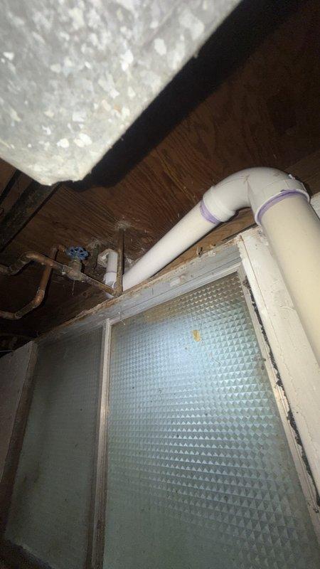 Replaced the complete kitchen drain stack from underneath the sink through to the main cleanout. Removed existing deteriorated piping and installed new white PVC drain line with proper pitch and support throughout the vertical run. The installation required opening wall access to expose the plumbing chase and connecting the new stack to existing supply lines and shutoff valves. Installed new braided flexible supply lines with chrome fittings and red-handled shutoff valve for water control. Secured all piping to structural framing per code requirements and routed the drain stack through the basement area past the glass block window to connect with the main cleanout. All connections were tested for proper drainage and leak-free operation before completion.
