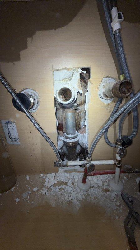 Replaced the complete kitchen drain stack from underneath the sink through to the main cleanout. Removed existing deteriorated piping and installed new white PVC drain line with proper pitch and support throughout the vertical run. The installation required opening wall access to expose the plumbing chase and connecting the new stack to existing supply lines and shutoff valves. Installed new braided flexible supply lines with chrome fittings and red-handled shutoff valve for water control. Secured all piping to structural framing per code requirements and routed the drain stack through the basement area past the glass block window to connect with the main cleanout. All connections were tested for proper drainage and leak-free operation before completion.