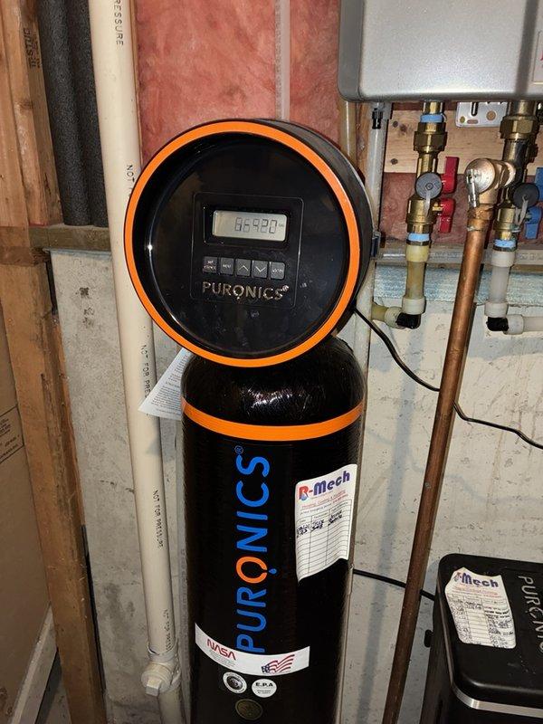 Performed routine maintenance inspection on Puronics water treatment system. Verified proper operation of control head unit displaying cycle information, checked system settings, and documented current installation configuration including all plumbing connections, valves, and associated mechanical equipment in utility area.