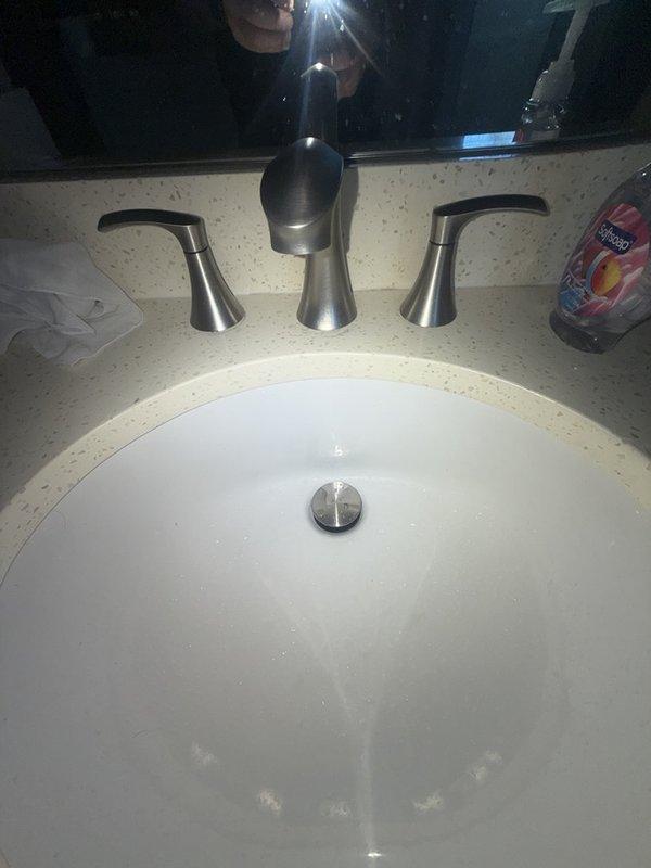 Responded to callback for worsening water pressure issue at bathroom sink. Upon arrival, inspected three-piece faucet assembly with center dome spout and dual lever handles in brushed nickel finish. Evaluated water flow from faucet and examined installation for potential causes of decreased pressure following previous service visit. Documented existing faucet configuration and undermount sink setup with photographic evidence for service records. Identified issue requiring further diagnosis of supply line restrictions or aerator blockage affecting water delivery to fixtures.