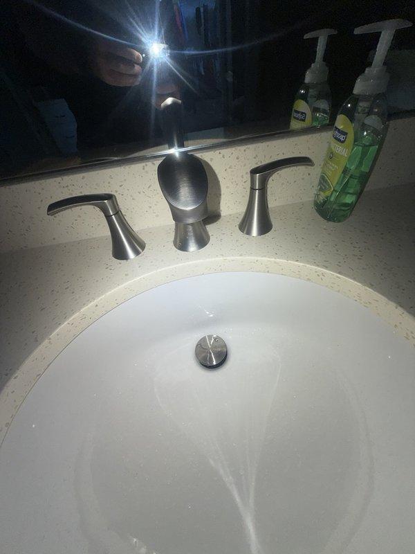 Responded to callback for worsening water pressure issue at bathroom sink. Upon arrival, inspected three-piece faucet assembly with center dome spout and dual lever handles in brushed nickel finish. Evaluated water flow from faucet and examined installation for potential causes of decreased pressure following previous service visit. Documented existing faucet configuration and undermount sink setup with photographic evidence for service records. Identified issue requiring further diagnosis of supply line restrictions or aerator blockage affecting water delivery to fixtures.