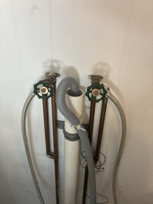 Prepared estimate for installation of two customer-supplied stem valves on the back porch water supply system. Assessed existing plumbing configuration consisting of two copper supply lines with shut-off valves featuring green handles, flexible braided metal supply lines, and gray corrugated flexible hose secured to wall with mounting brackets. Documented current condition of washing machine hookup connections and valve assembly through photographs for accurate quote preparation.