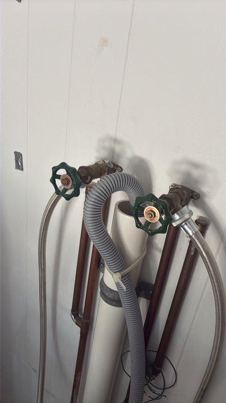 Prepared estimate for installation of two customer-supplied stem valves on the back porch water supply system. Assessed existing plumbing configuration consisting of two copper supply lines with shut-off valves featuring green handles, flexible braided metal supply lines, and gray corrugated flexible hose secured to wall with mounting brackets. Documented current condition of washing machine hookup connections and valve assembly through photographs for accurate quote preparation.