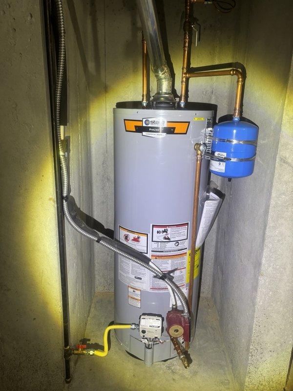 Responded to water treatment assistance request in basement utility area. Inspected residential water heater system including copper supply lines, expansion tank, gas connections, and dual ball valve assembly. Documented complete installation setup showing proper expansion tank mounting, gas line configuration with yellow supply piping, red circulation pump assembly, and water heater specifications. Verified all plumbing connections, valve operations, and system components for proper water treatment functionality and safety compliance.