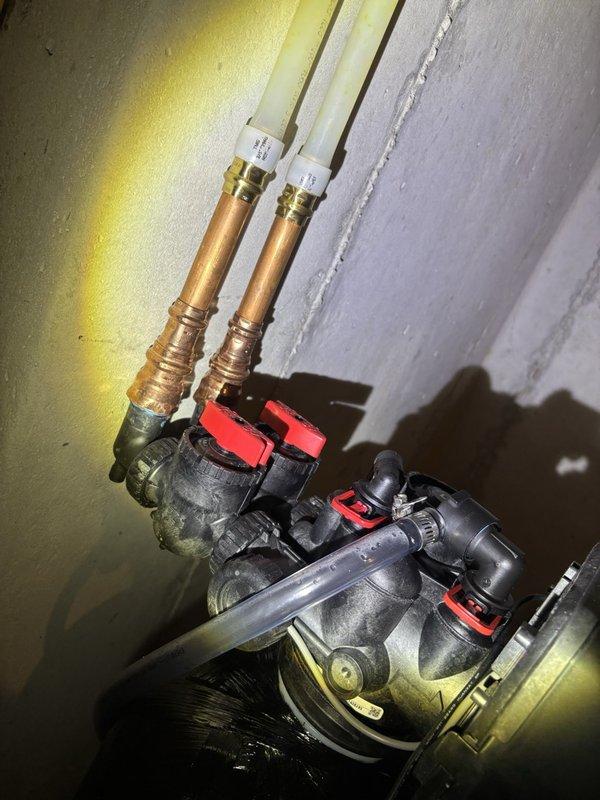Responded to water treatment assistance request in basement utility area. Inspected residential water heater system including copper supply lines, expansion tank, gas connections, and dual ball valve assembly. Documented complete installation setup showing proper expansion tank mounting, gas line configuration with yellow supply piping, red circulation pump assembly, and water heater specifications. Verified all plumbing connections, valve operations, and system components for proper water treatment functionality and safety compliance.
