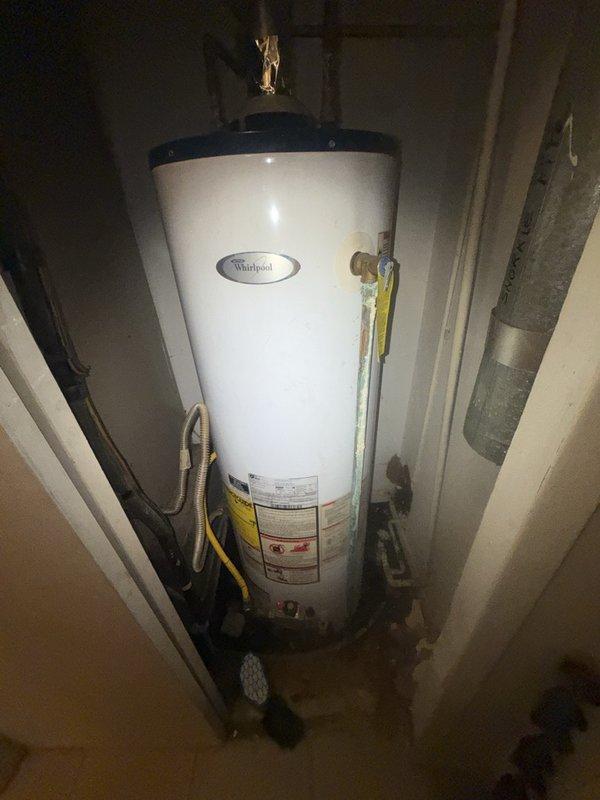 Responded to report of water leak in furnace closet extending into hallway. Upon inspection, identified source as Whirlpool water heater with failed connection or component causing water discharge. Documented conditions showing accumulated debris and moisture damage in confined mechanical space between HVAC equipment and wall. Inspected water heater plumbing connections including brass fittings, copper supply lines, and yellow flexible gas line for integrity. Assessed surrounding area for water damage and verified proper drainage. Photographed equipment installation, connection points, and affected areas for service records. Recommended appropriate repairs to resolve active leak and prevent further water intrusion into living space.