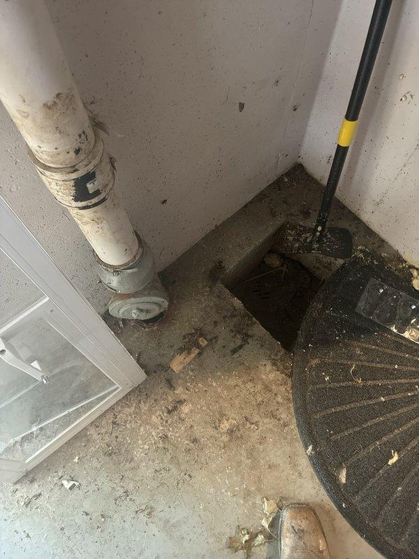 Performed camera inspection of main drain line in basement to assess reported breaks and determine repair or replacement requirements. Documentation revealed significant deterioration at pipe penetration point through floor with visible structural damage to concrete and exposed void beneath foundation. Sump pump pit area inspected showing standing water and evidence of chronic moisture issues with surrounding floor surfaces displaying extensive water damage, soil accumulation, and debris. Photographed vertical drain stack showing advanced deterioration with compromised pipe integrity and floor drain connections. Assessment indicates main line damage requiring excavation and replacement, with additional evaluation needed for potential washing machine drain line installation to address drainage deficiencies contributing to observed water infiltration and basement flooding conditions.
