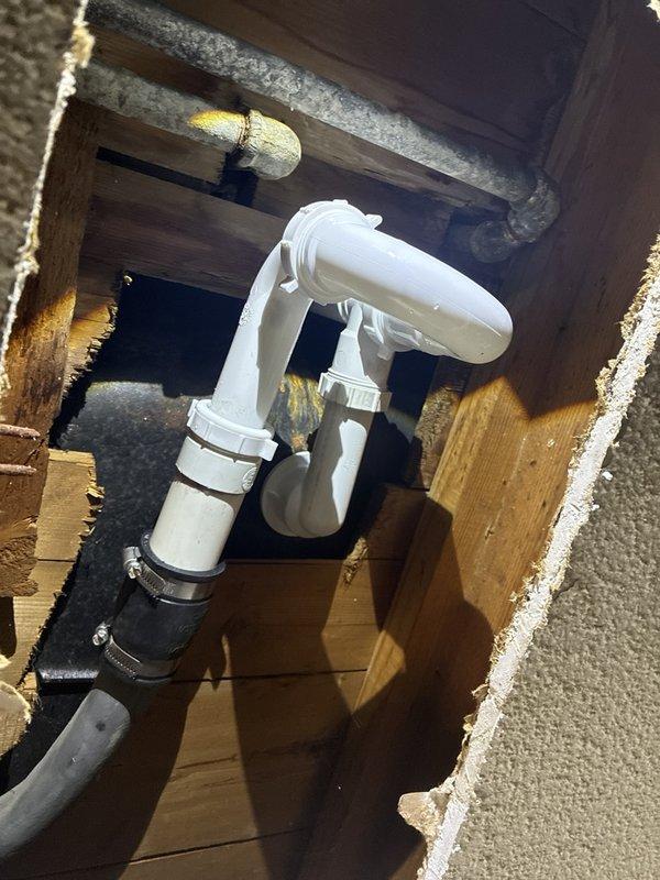 Responded to water leak in laundry room ceiling with unknown source. Accessed attic space above affected area and located compromised PVC drain line with failing coupling connection at P-trap assembly. Removed defective rubber coupling with deteriorated clamps and replaced with properly secured connection using appropriate fittings. Inspected surrounding plumbing infrastructure including adjacent black drainage pipe secured with metal clamp to wooden framing. Verified all connections were watertight and properly supported. Documented conditions with photos showing repair area and surrounding attic space with insulation.