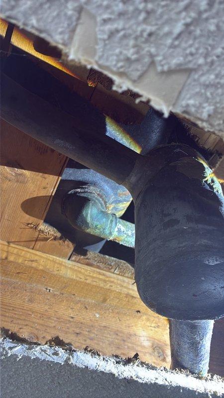 Responded to water leak in laundry room ceiling with unknown source. Accessed attic space above affected area and located compromised PVC drain line with failing coupling connection at P-trap assembly. Removed defective rubber coupling with deteriorated clamps and replaced with properly secured connection using appropriate fittings. Inspected surrounding plumbing infrastructure including adjacent black drainage pipe secured with metal clamp to wooden framing. Verified all connections were watertight and properly supported. Documented conditions with photos showing repair area and surrounding attic space with insulation.