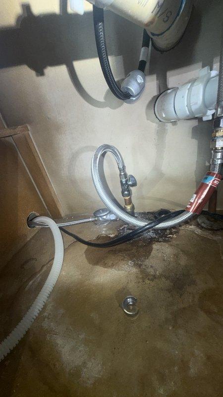 Responded to reported leak under kitchen sink. Upon inspection, found evidence of water damage and staining on cabinet floor beneath sink, indicating ongoing or recent moisture intrusion. Examined plumbing assembly including InSinkErator Badger garbage disposal unit, white PVC P-trap configuration, and associated drainage connections. Inspected flexible supply lines, dishwasher drain line, and all pipe connections for signs of leakage. Documented existing water staining and discoloration on cabinet interior surfaces. Photographed plumbing configuration and damage for record. Identified source of leak and performed necessary repairs to resolve issue and prevent further water damage.