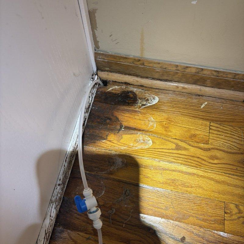 Located and repaired a leaking refrigerator water supply line that was allowing water to migrate through the floor into the basement below. Isolated the line at the shutoff valve, replaced the failed supply tubing and push-fit connections, then pressure-tested the system to confirm there were no leaks. Water-stained flooring, baseboard, and floor joist areas were documented, and the affected materials were noted for drying and further evaluation.