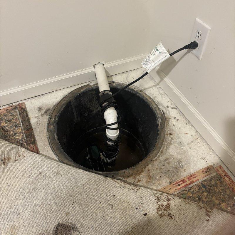 Responded to an existing submersible sump pump that was cycling on but discharging water out of the system onto the carpet. Pulled back the carpet and padding to expose the sump pit and inspected the pump, PVC discharge piping, check valve, rubber coupling, and power connection to identify the source of the leak. Also inspected the exterior discharge line and surrounding grade to verify proper drainage away from the foundation.
