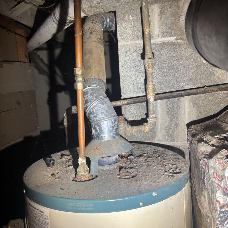 Assessed a water leak at the cast iron drain stack and documented significant pooling, rust staining, and moisture damage on the surrounding concrete floor. Inspected adjacent piping and equipment, including the gas water heater, its flue vent, and corroded supply and gas line fittings, and prepared an estimate for the necessary stack repair.