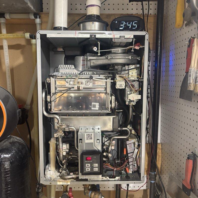 Diagnosed a tankless water heater cycling off shortly after reset with recurring error code 11 (ignition failure). Removed the front cover and inspected the ignition electrode, flame rod, and burner assembly, finding soot and corrosion deposits on the stainless burner panel that were interfering with ignition and flame sensing. Cleaned the affected components and reassembled the unit.