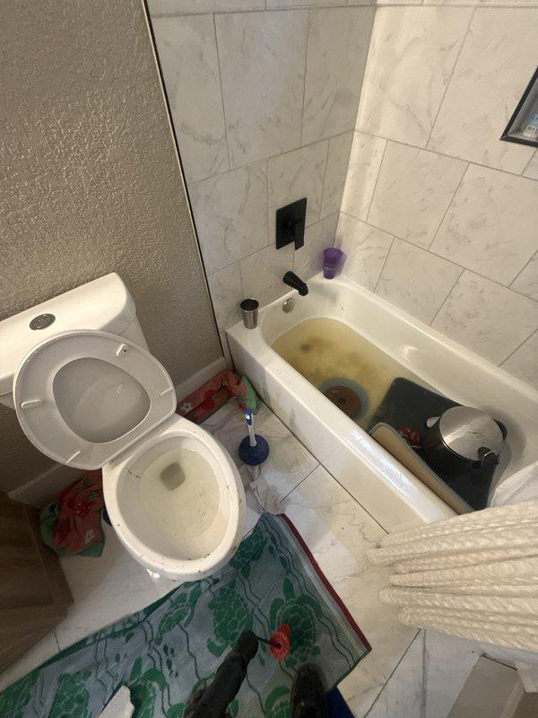 Responded to a main sewer line backup with the bathroom tub and toilet overflowing and multiple fixtures draining slowly. Pulled the toilet to gain direct access to the closet flange and fed a drain-cleaning cable through the opening to clear the blockage in the main line, restoring flow to the affected fixtures. The toilet was then ready to be reset on the flange with the water supply line reconnected.