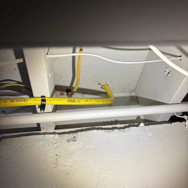 Assessed the gas supply for the new range, where a yellow corrugated flexible gas connector runs overhead through the joist space to a shutoff valve with threaded black iron fittings showing light surface corrosion and rust staining at the joints. Evaluated replacement of the flexible connector with a rigid gas pipe run and reviewed the refrigerator water supply, where the existing T-valve would need to be replaced with a proper dedicated shutoff for the ice maker/water line hookup. Documented existing conditions with photos and prepared the scope of work for the fixture installation estimate.