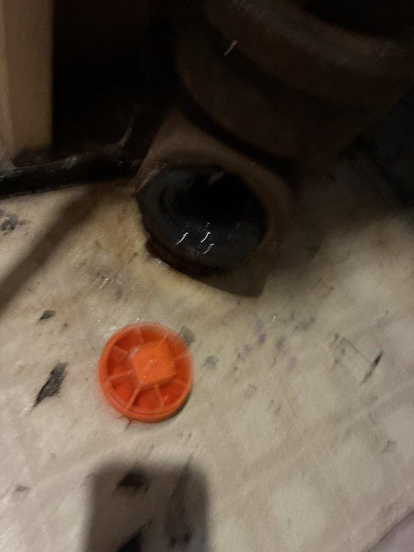 Responded to a callback for a dislodged cleanout cap on the main drain line, which was allowing wastewater to discharge onto the floor whenever fixtures were in use. Inspected the open cleanout and found the cap and its sealing gasket had failed, with the gasket cracked and broken and the threaded fitting heavily corroded. Cleaned up the discharged wastewater and restored the main drain to proper operation, and recommended a camera inspection of the line given the history of recurring clogs.