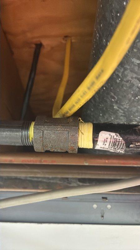 Performed a gas leak inspection and pressure test on the gas piping serving the stove, focusing on the reported area in the basement ceiling near the shut-off valve. Inspected the black iron piping, threaded cast-iron couplings and elbow fittings, and the yellow flexible gas lines, noting surface corrosion on the threaded joints, which were wrapped with thread-seal tape. Gas remained off during the inspection, and the piping was left ready for any needed repair.