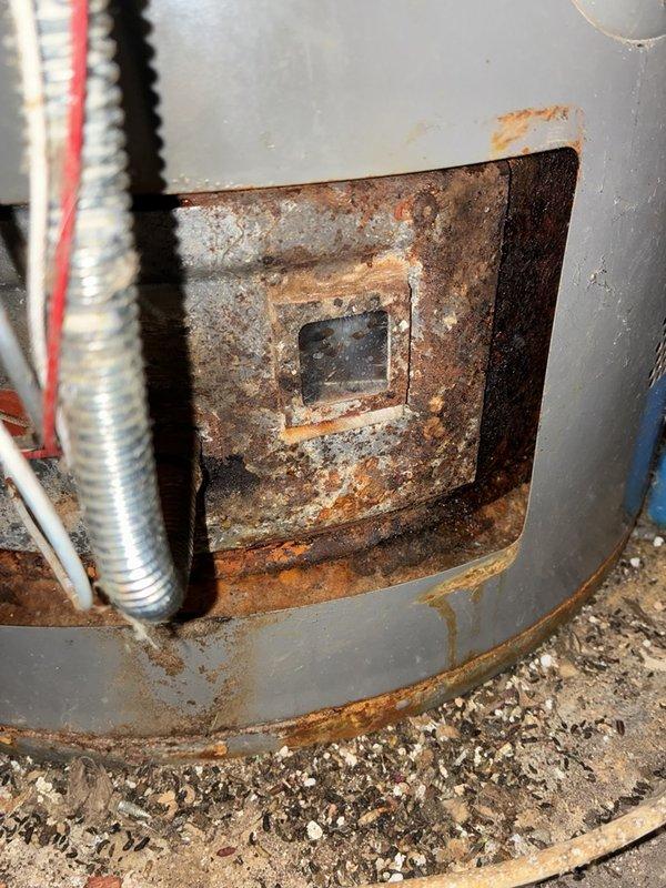 Diagnosed a gas-fired tank water heater with no hot water and found severe corrosion and heavy rust buildup at the burner compartment access opening and along the lower tank jacket, along with sediment and debris around the burner observation port and gas supply line. The unit's advanced corrosion and deteriorated condition were documented with photos, and replacement is recommended in lieu of repair.