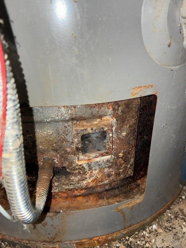 Diagnosed a gas-fired tank water heater with no hot water and found severe corrosion and heavy rust buildup at the burner compartment access opening and along the lower tank jacket, along with sediment and debris around the burner observation port and gas supply line. The unit's advanced corrosion and deteriorated condition were documented with photos, and replacement is recommended in lieu of repair.