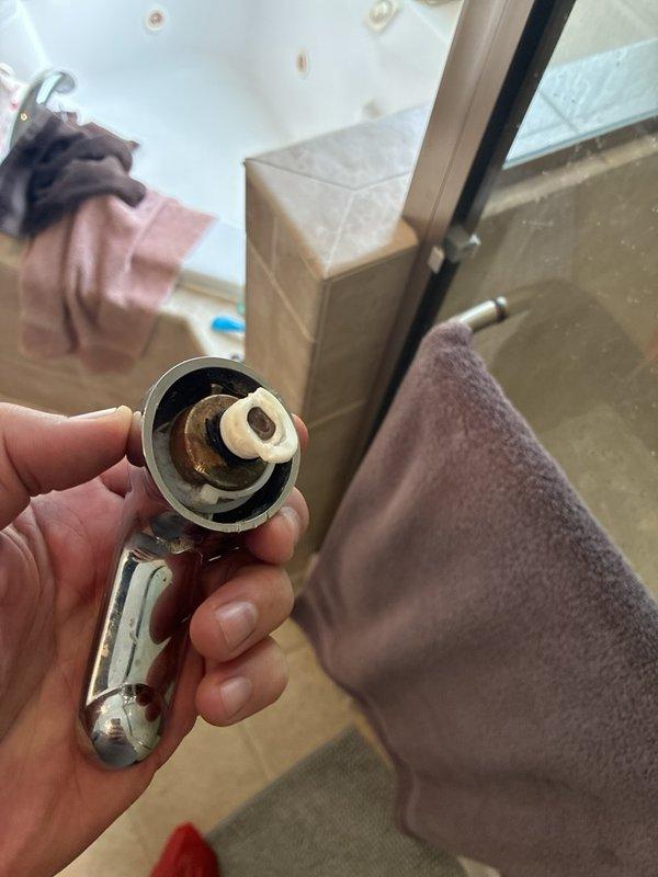 Diagnosed a leaking master shower faucet and removed the handle, revealing a degraded, deformed plastic stem adapter and mineral buildup around the valve stem. The aged valve cartridge, estimated at 20 years old, appears to have failed, but the valve could not be removed for further inspection. The shower supply was capped to stop the leak, and cartridge or valve replacement is recommended.