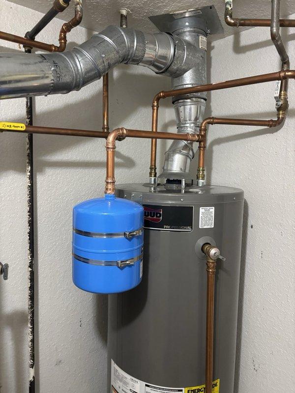 Inspected the gas-fired tanked water heater for a leaking temperature and pressure (T&P) relief valve discharge pipe. Verified static system pressure at approximately 70–75 PSI using a gauge at the drain valve, and confirmed the thermal expansion tank is installed and secured with clamps, with no visible corrosion, rust, or damage at the connections. Findings indicate the relief valve discharge is likely related to thermal expansion and elevated system pressure.