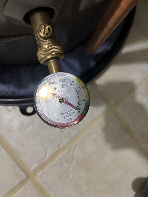 Inspected the gas-fired tanked water heater for a leaking temperature and pressure (T&P) relief valve discharge pipe. Verified static system pressure at approximately 70–75 PSI using a gauge at the drain valve, and confirmed the thermal expansion tank is installed and secured with clamps, with no visible corrosion, rust, or damage at the connections. Findings indicate the relief valve discharge is likely related to thermal expansion and elevated system pressure.