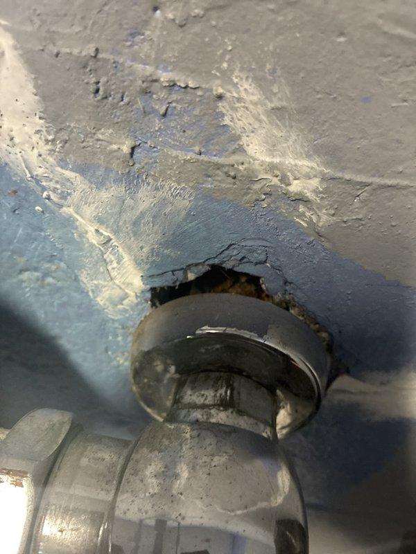 Performed a plumbing estimate to evaluate and scope repairs for reported leaks. Inspected supply and drain piping in the basement/crawlspace area, documenting a broken-out opening in the concrete block wall with pipe penetrations and fittings, corroded piping and a valve, and a PVC drain stub with a threaded coupling that is open and contaminated with debris. Also identified a tarnished chrome pipe fitting with escutcheon at a ceiling/wall penetration where deteriorated sealant and failed surface material have created a gap, indicating a probable leak source requiring repair.