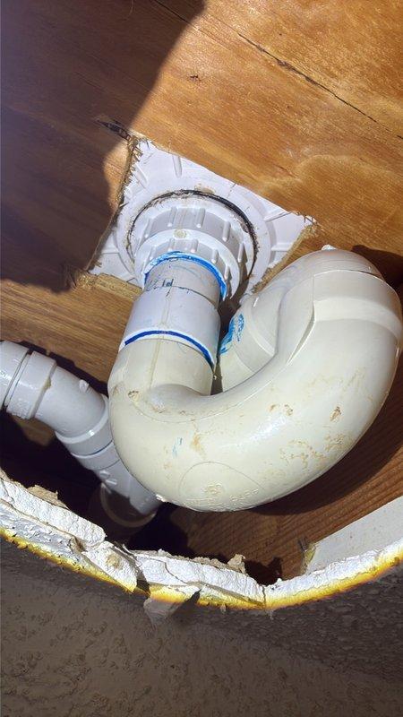 Repaired a leaking shower drain by accessing the PVC drain assembly from below through the existing garage ceiling opening. Inspected the P-trap, vertical riser, and flanged drain fitting seated in the subfloor, then serviced the connections and sealing at the drain flange to eliminate the leak.