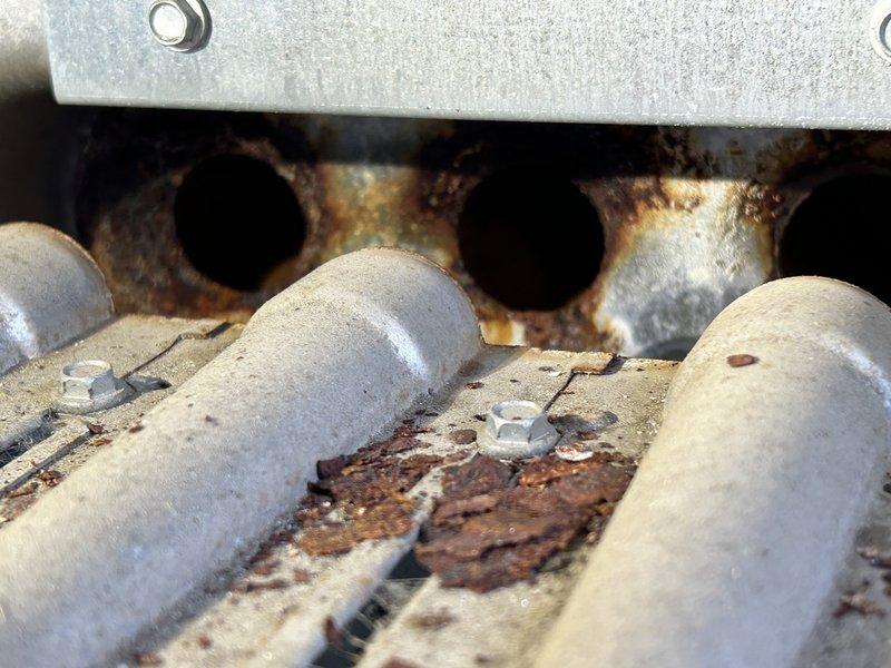 Inspected two rooftop units (RTUs) on south end of building for reported heating failure. Visual examination confirmed significant rust and corrosion on the heat exchanger burner components, with severe oxidation evident on metal surfaces, burner tubes, and manifold openings. Findings support previous diagnosis of deteriorated heat exchanger requiring replacement.