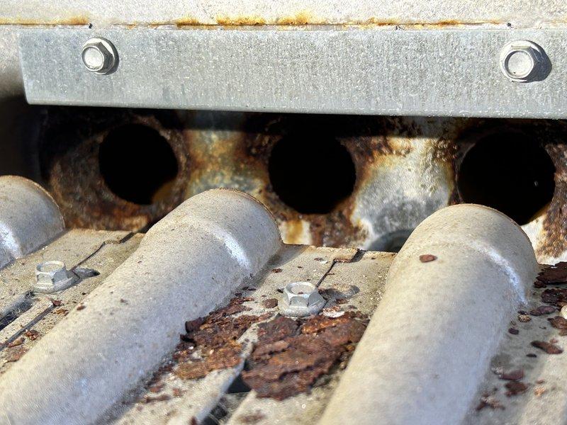 Inspected two rooftop units (RTUs) on south end of building for reported heating failure. Visual examination confirmed significant rust and corrosion on the heat exchanger burner components, with severe oxidation evident on metal surfaces, burner tubes, and manifold openings. Findings support previous diagnosis of deteriorated heat exchanger requiring replacement.