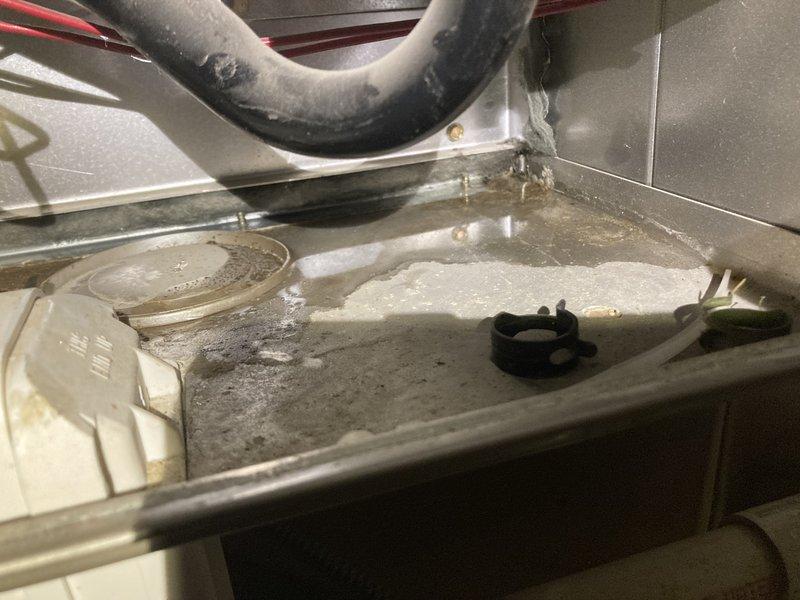 Responded to service call for water leakage under furnace. Inspection revealed condensation water leaking from heat exchanger with significant mineral buildup and corrosion in the drain pan. Discovered moisture damage affecting nearby insulation, indicated by rust-colored staining on the vapor barrier.