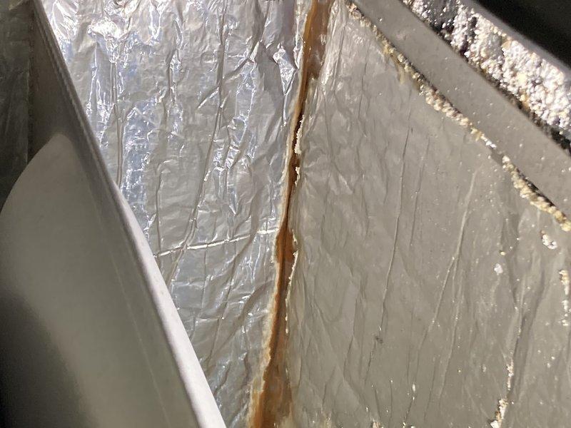 Responded to service call for water leakage under furnace. Inspection revealed condensation water leaking from heat exchanger with significant mineral buildup and corrosion in the drain pan. Discovered moisture damage affecting nearby insulation, indicated by rust-colored staining on the vapor barrier.