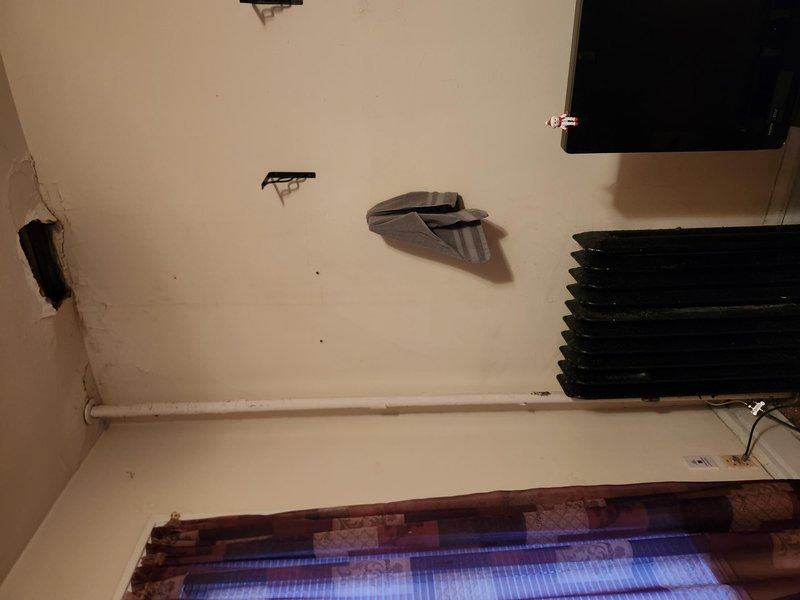 Investigated ceiling leak reported by resident that occurs intermittently with radiator "clanking" sounds. Accessed the site using provided lockbox codes and inspected the existing ceiling opening. Enlarged the access hole to better examine plumbing infrastructure and identified water damage consistent with an intermittent supply line leak. Repaired the compromised pipe connection and documented the condition with photos showing the extent of ceiling damage and affected wall areas.