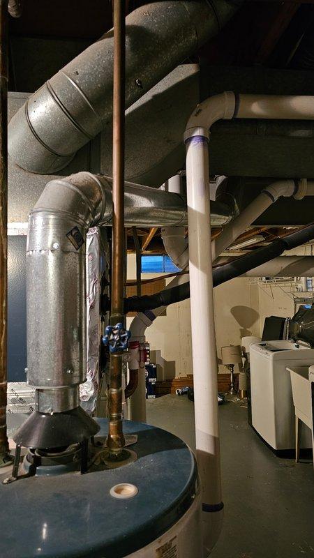 Conducted comprehensive assessment of aging water heater system requiring replacement. Inspected existing installation including metal T-junction ductwork showing corrosion at connection points and evaluated current ventilation configuration. Documented condition of utility room setup with existing galvanized metal ducts, copper piping, and PVC drainage components to prepare detailed replacement estimate.