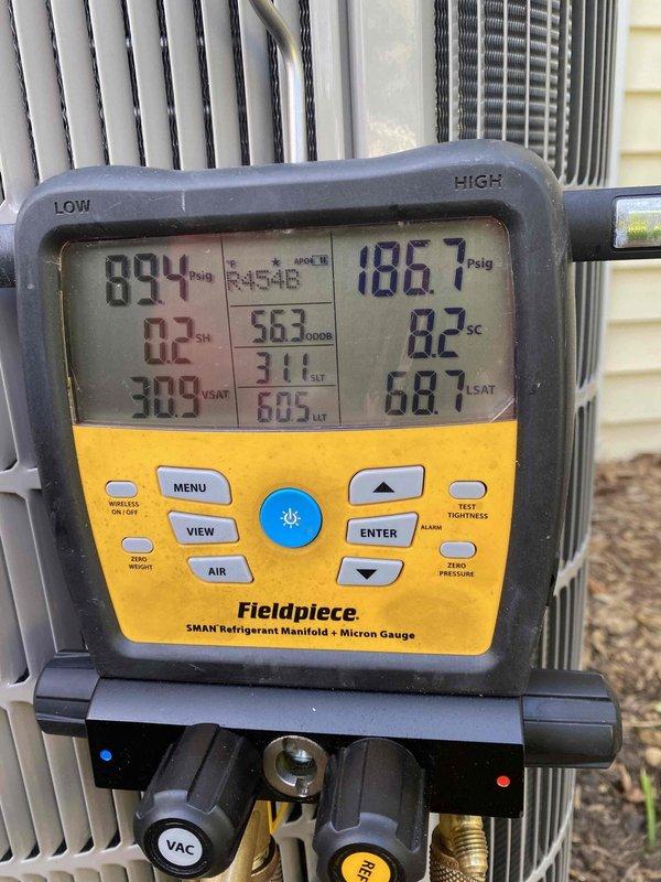 Performed diagnostic testing on outdoor HVAC unit using Fieldpiece SMAN refrigerant manifold and micron gauge. Recorded system pressures at 89.4 PSig low side and 186.7 PSig high side, with subcooling measured at 82°F. Inspected rigid foam insulation board near equipment foundation area and documented measurements marked on material for spring NESU installation requirements.