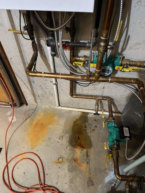 Responded to maintenance callback for water leak originating from boiler system. Upon inspection, identified active leakage evidenced by rust-colored staining on concrete floor surrounding boiler piping connections. Inspected all copper piping, ball valves, flexible metallic conduits, and heat exchanger components for source of leak and verified proper operation of system following previous maintenance service performed earlier this season.