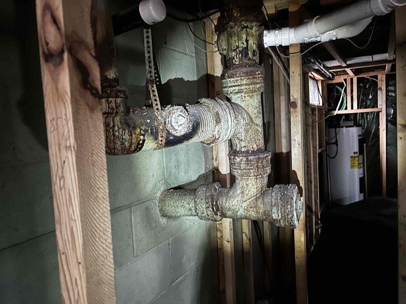 Inspected property after house fire to provide quotation for replacement of severely corroded cast iron drain lines and damaged water supply piping. Documented extensive deterioration at pipe joints with visible white-green mineral deposits and rust throughout the basement plumbing system. Water heater remains in good condition and was not included in replacement estimate.