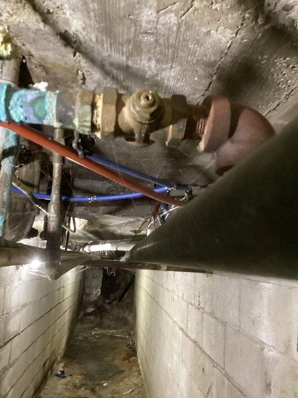 Investigated water leak in basement area. Identified significant corrosion and active leak at copper pipe elbow joint showing turquoise patina. Repaired corroded copper fitting in confined utility space where multiple supply lines run along concrete ceiling structure.